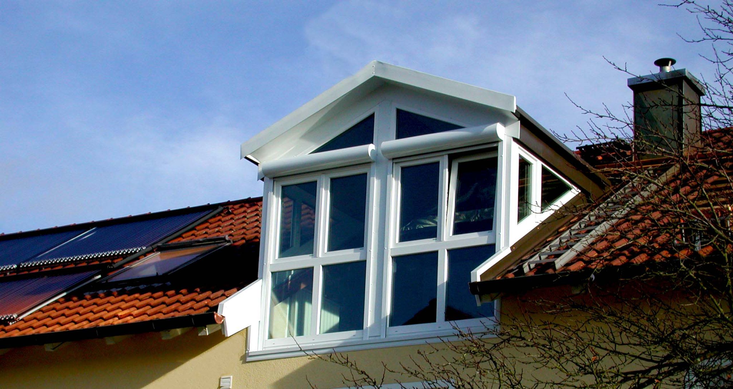 In ein Münchener Wohnhaus eingebaute Dachgaube mit weißem Spitzdach und Fensterrahmen